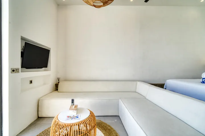 Close view of a low white sectional and woven coffee table, with the edge of a bed at right.