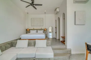 Low bed behind a sectional sofa, with arched niches and a ceiling fan.