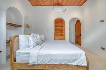 Bedroom with white bedding, arched wood door and pale built-in wall niches.