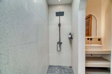 Walk-in shower with dark shower fittings beside a small stone vanity and arched mirror.