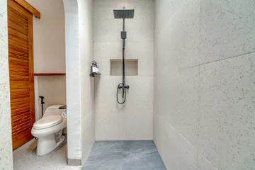 Tiled shower enclosure with dark shower fittings beside a partial view of the toilet.