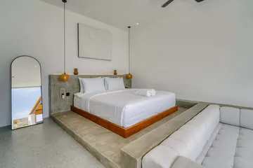 Bedroom with white bed and sectional beneath a ceiling fan and woven pendants.