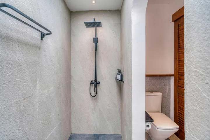 Walk-in shower with pale stone walls and dark shower fixture.