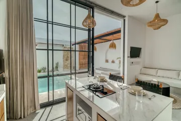 Kitchen island with cooktop and place settings beside black-framed glass doors, with the sectional sofa beyond.