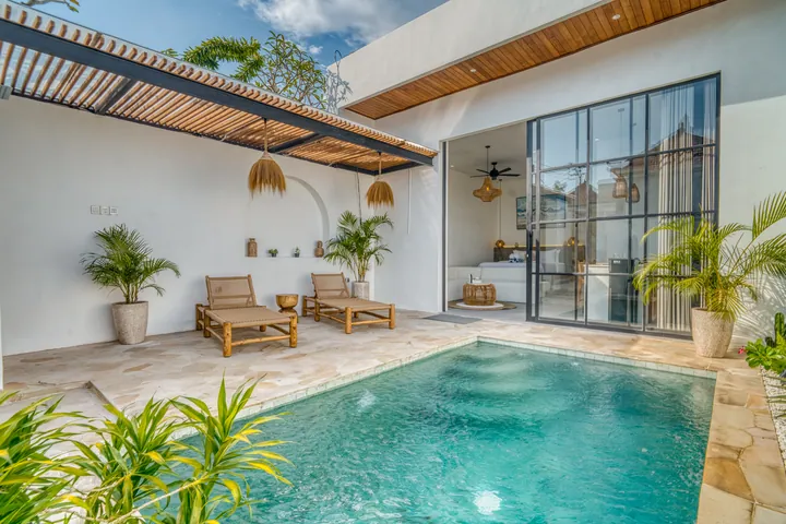 Pool courtyard with pale paving, loungers and glass doors beneath timber shade.