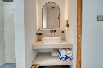 An arched bathroom mirror above a stone basin and folded towels.