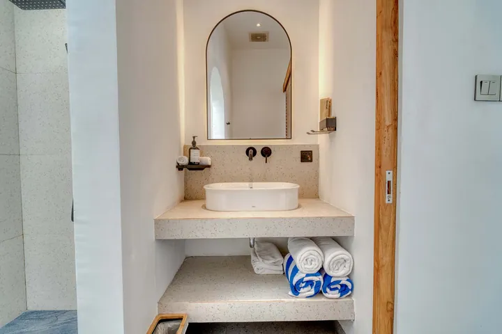 An arched bathroom mirror above a stone basin and folded towels.