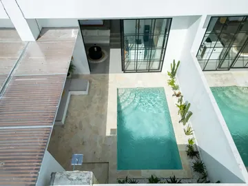 Aerial view down into a narrow courtyard pool between pale stone decks and roof structures.