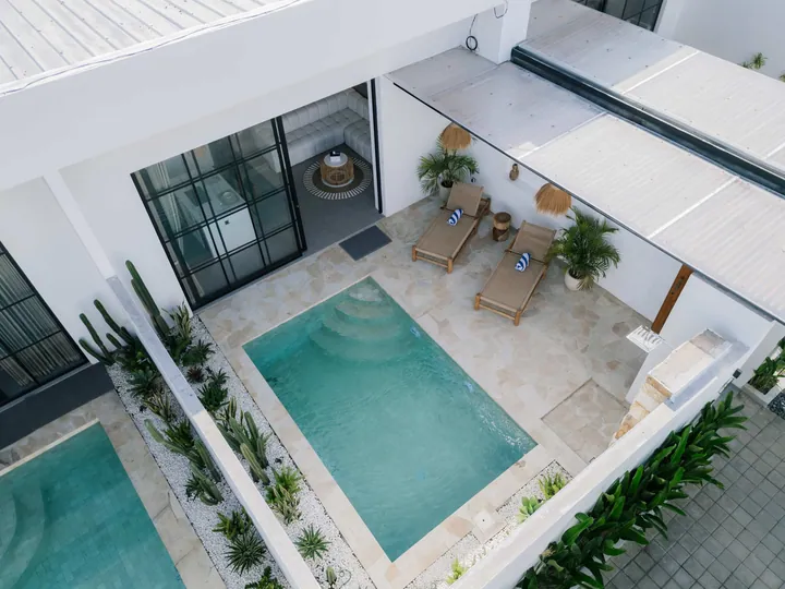 Aerial view down into a courtyard pool with stepped entry, loungers, planting and black-framed glazing.