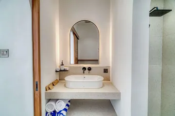 An arched bathroom mirror, pale stone basin and timber detailing.