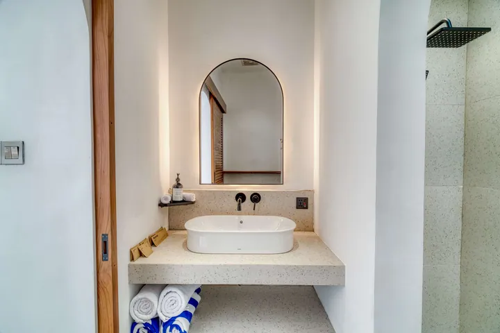 An arched bathroom mirror, pale stone basin and timber detailing.