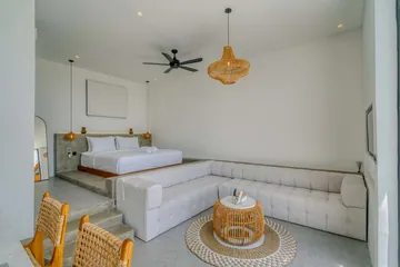 A white bed behind a pale sunken sofa, with a dining area to the left.