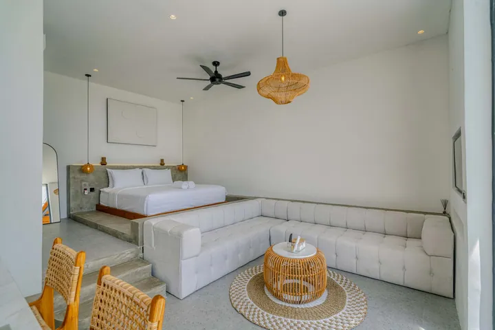 White sectional and bed in a bright room beneath woven pendant lights.