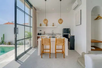 Kitchen and dining counter beside full-height glass doors and courtyard greenery.