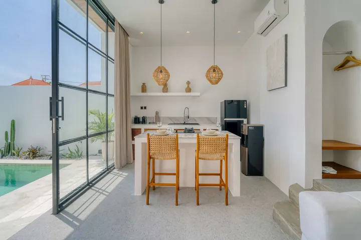 A kitchen island with timber stools beside tall glass doors and a sunlit pool.