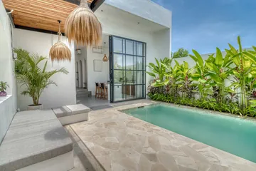 Sunlight crosses a pale courtyard beside a turquoise pool and tall green planting.