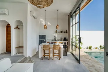 Glass-walled living and kitchen area opening toward a small turquoise pool and paved patio.
