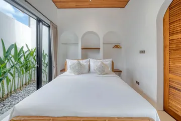 White bed with wood frame in a bright bedroom beside an arched wall niche.
