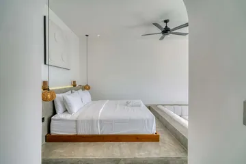 White bed on a low wood platform against a pale bedroom wall.