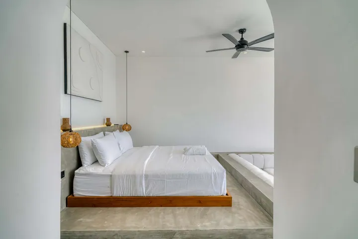 White bed on a low wood platform against a pale bedroom wall.