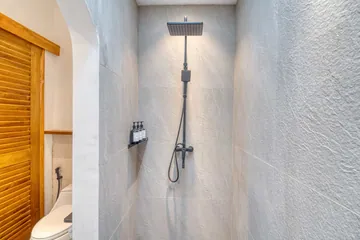 Close view of a tiled shower enclosure with rain-style showerhead and adjacent wooden louvered door.