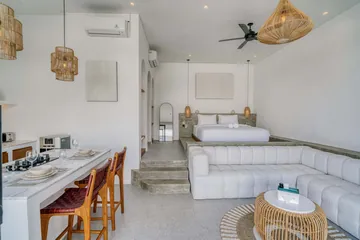 Open bedroom and lounge with white bed, sectional sofa and compact kitchen.