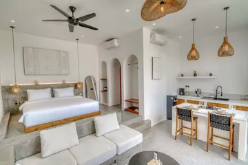 Open-plan room with a low bed, sectional sofa and kitchen counter with dark chairs.