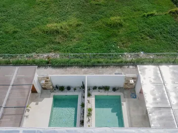 Aerial view of courtyard pools and low white villas beside green fields.