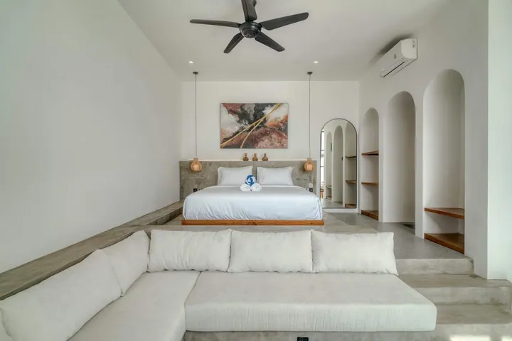 Low bed behind a sectional sofa, with arched niches and framed artwork above the bed.