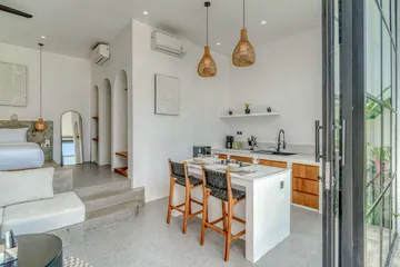 Open-plan room with kitchen counter, dining table and bed beyond the living area.