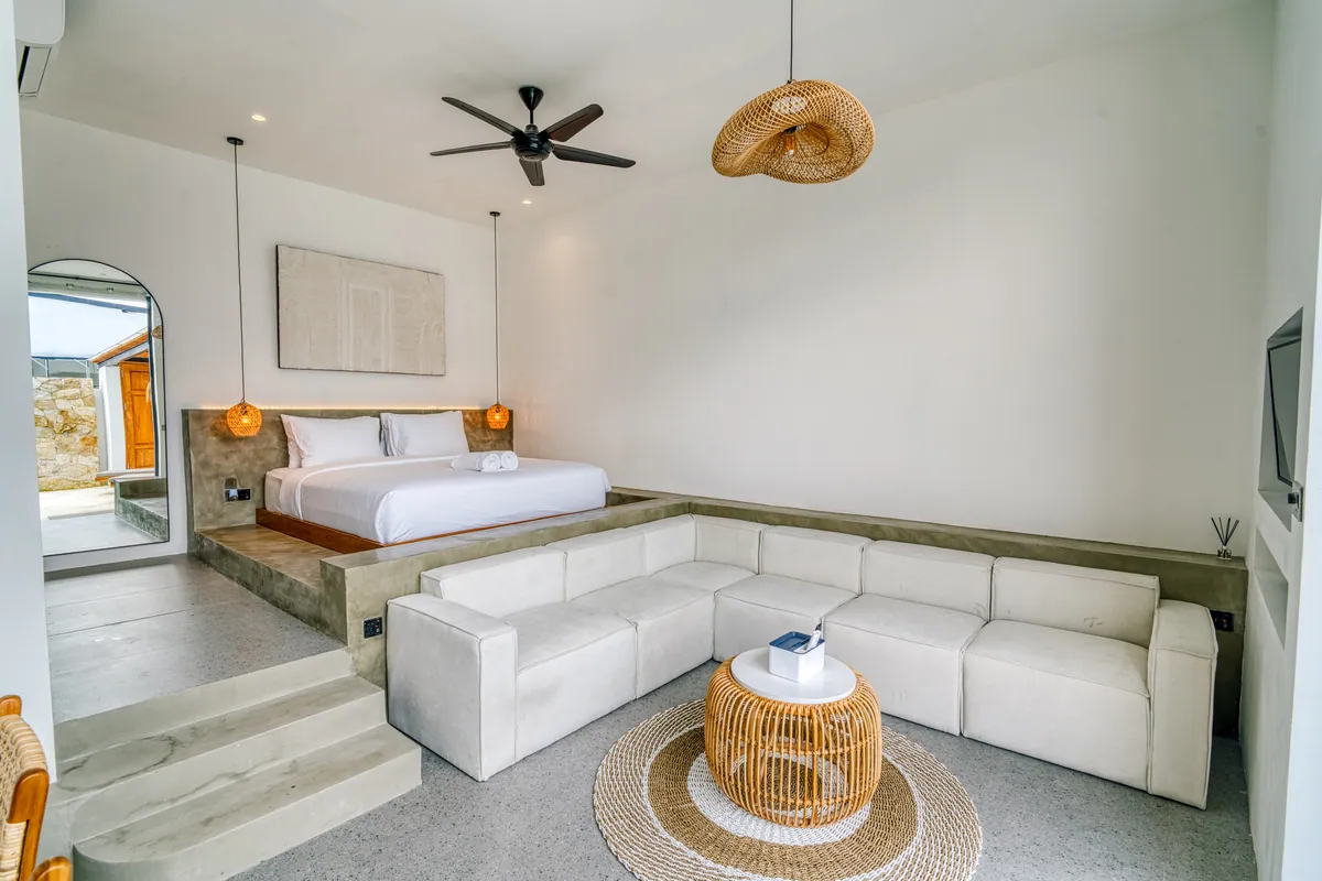 Low bed and pale sectional sofa beneath a ceiling fan, with arched wall niches along the side.