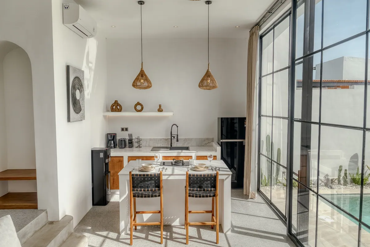 Kitchen with dark chairs and wood-front cabinetry, viewed beside the full-height glass wall.