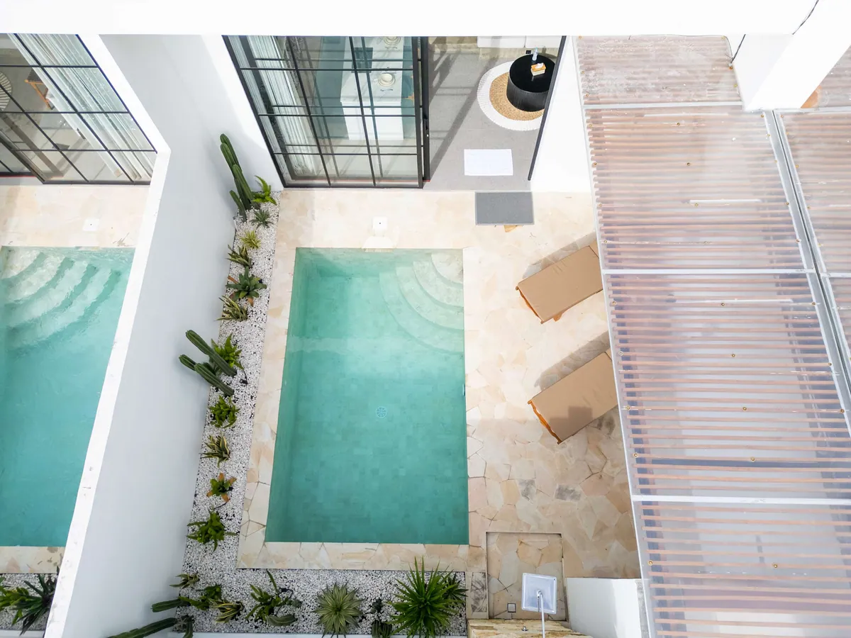 Top-down view of a courtyard pool with stepped entry, a cactus bed on white gravel, loungers and a slatted pergola.