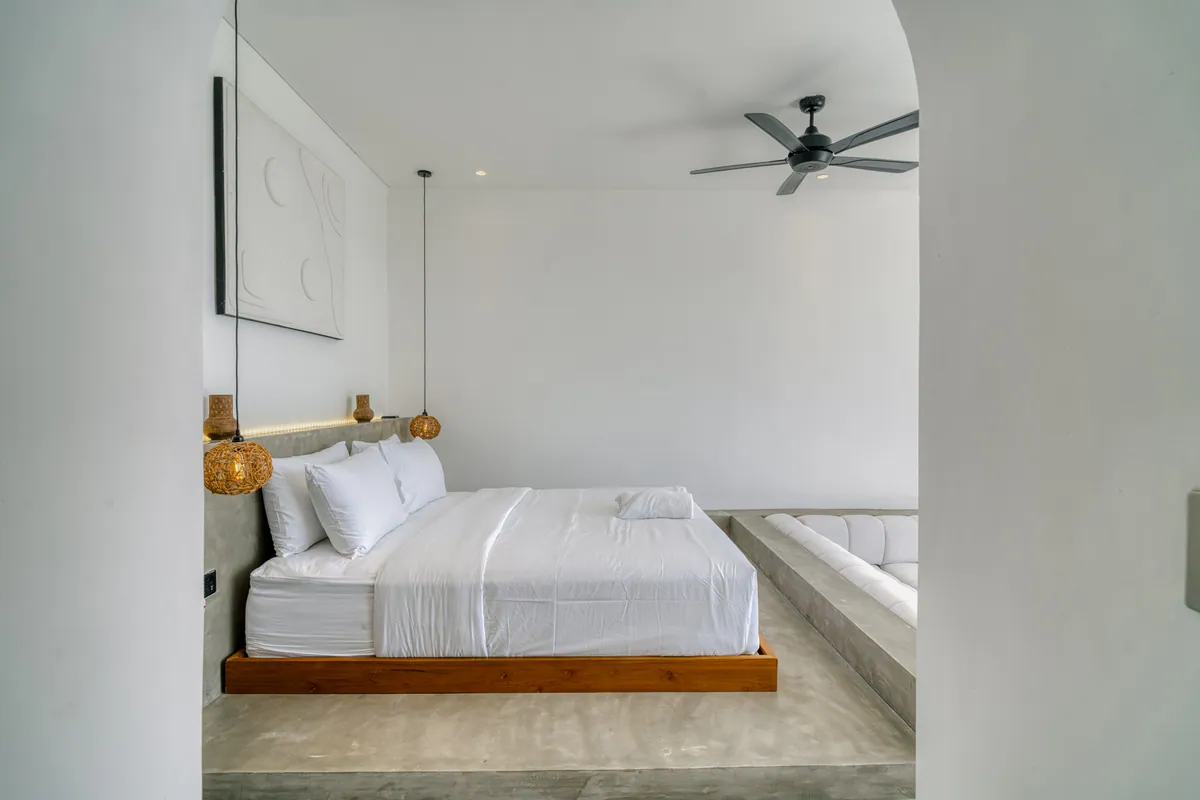 White bed on a low wood platform against a pale bedroom wall.