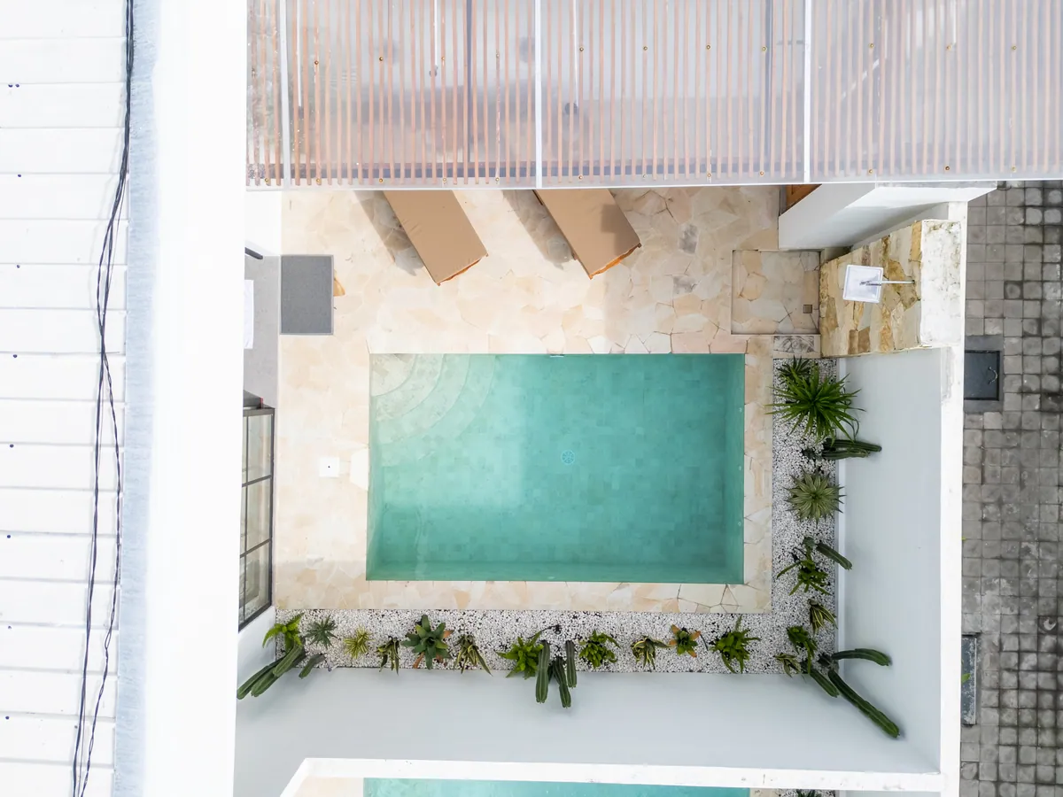 Top-down view of a courtyard pool with stone paving, planting and the edge of a slatted pergola.