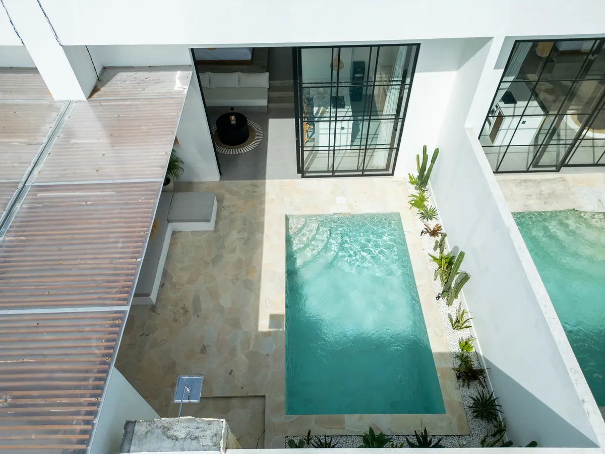 Aerial view down into a narrow courtyard pool between pale stone decks and roof structures.