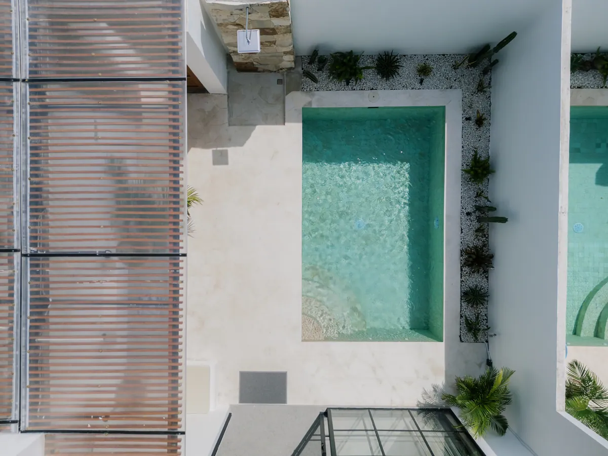 Overhead view of a narrow turquoise pool beside timber shade and pale paving.