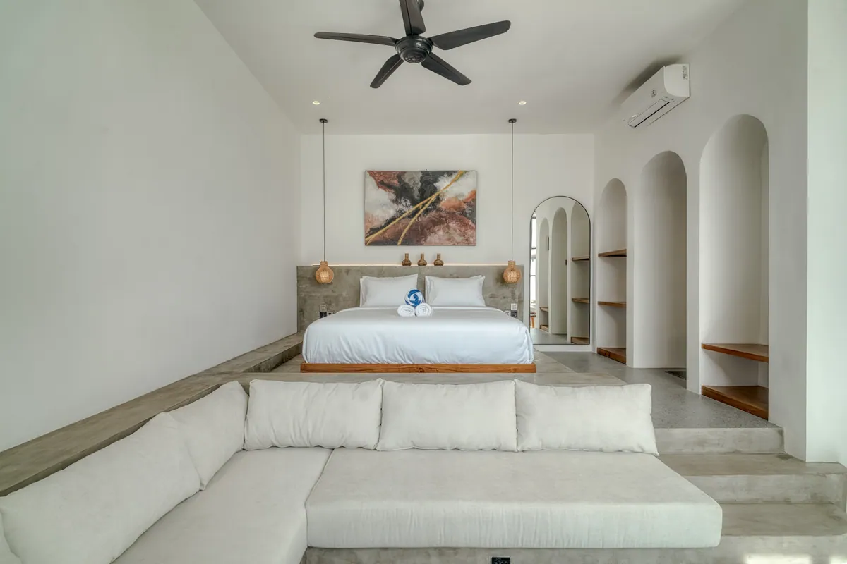 Low bed behind a sectional sofa, with arched niches and framed artwork above the bed.