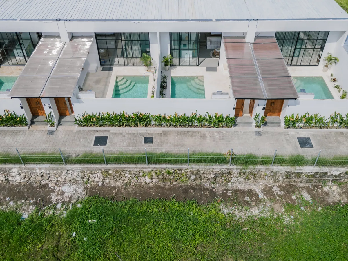 Aerial view of a white villa row and planted borders along a paved lane.