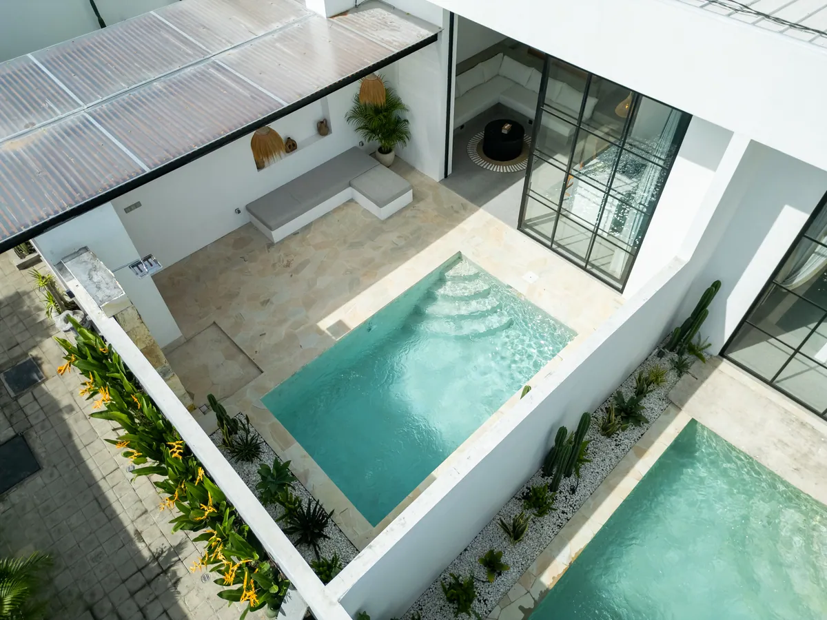 Aerial view down into a courtyard pool with stepped entry, stone deck, planting and black-framed glazing.