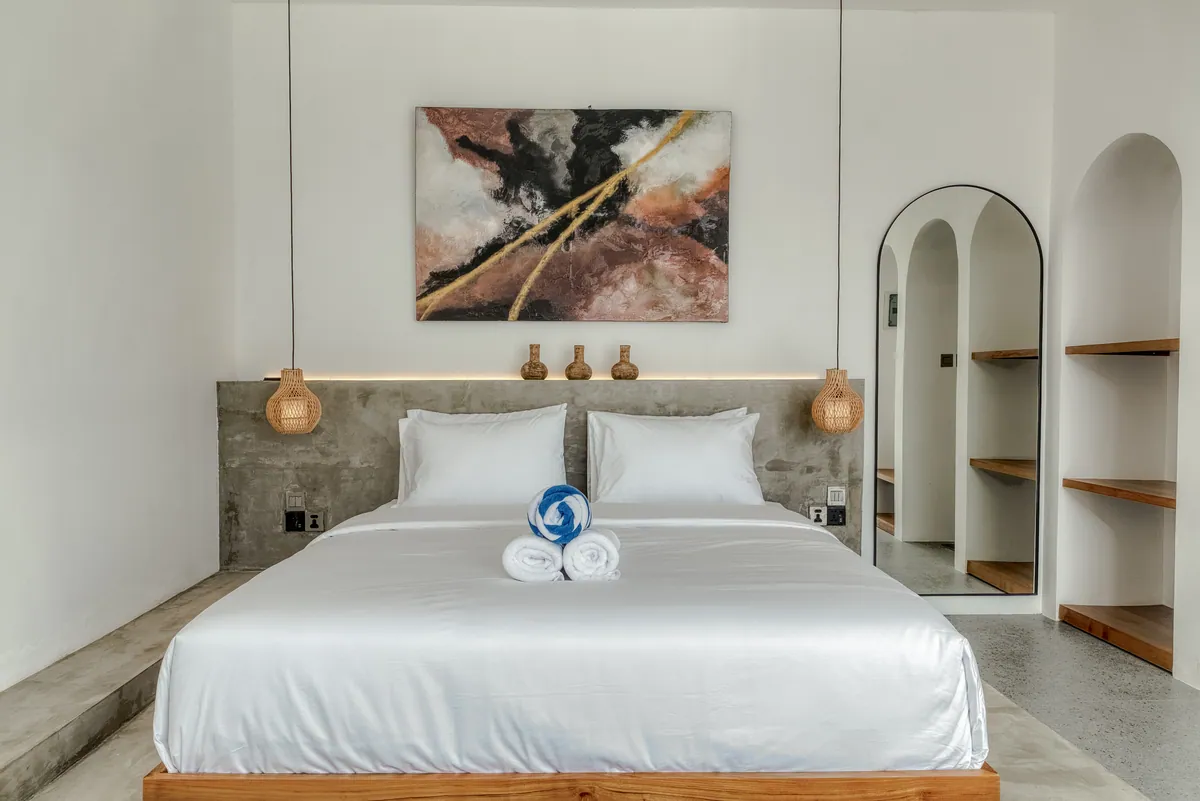 Close view of a made bed beneath abstract artwork, with arched wall niches and bedside pendants.