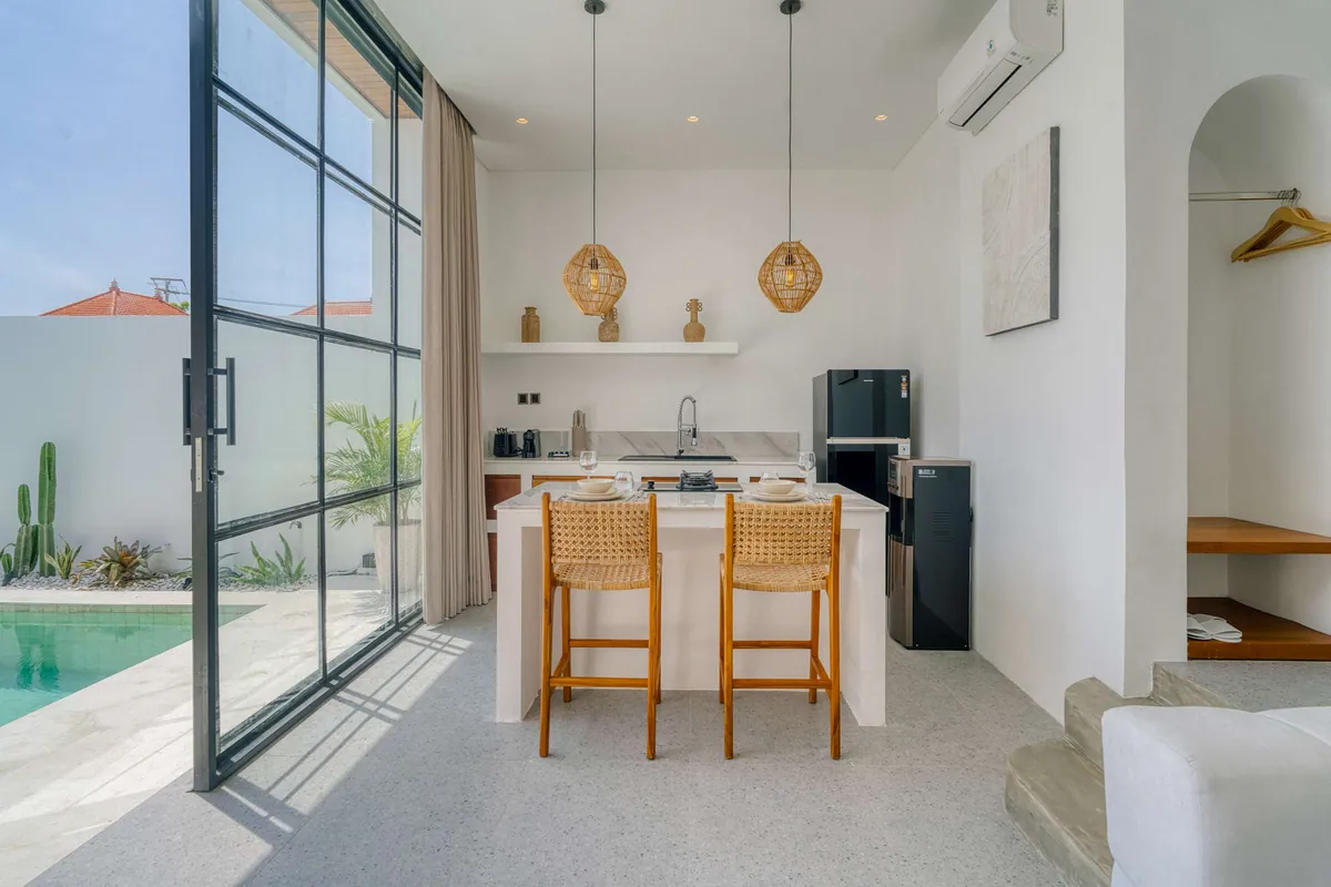 A kitchen island with timber stools beside tall glass doors and a sunlit pool.