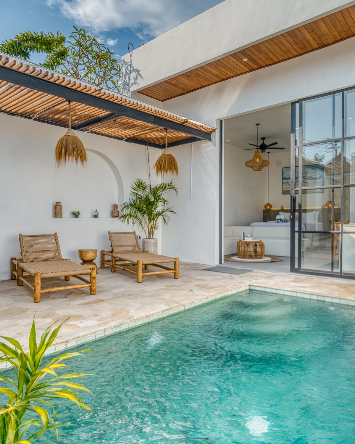 Pool courtyard with pale paving, loungers and glass doors beneath timber shade.
